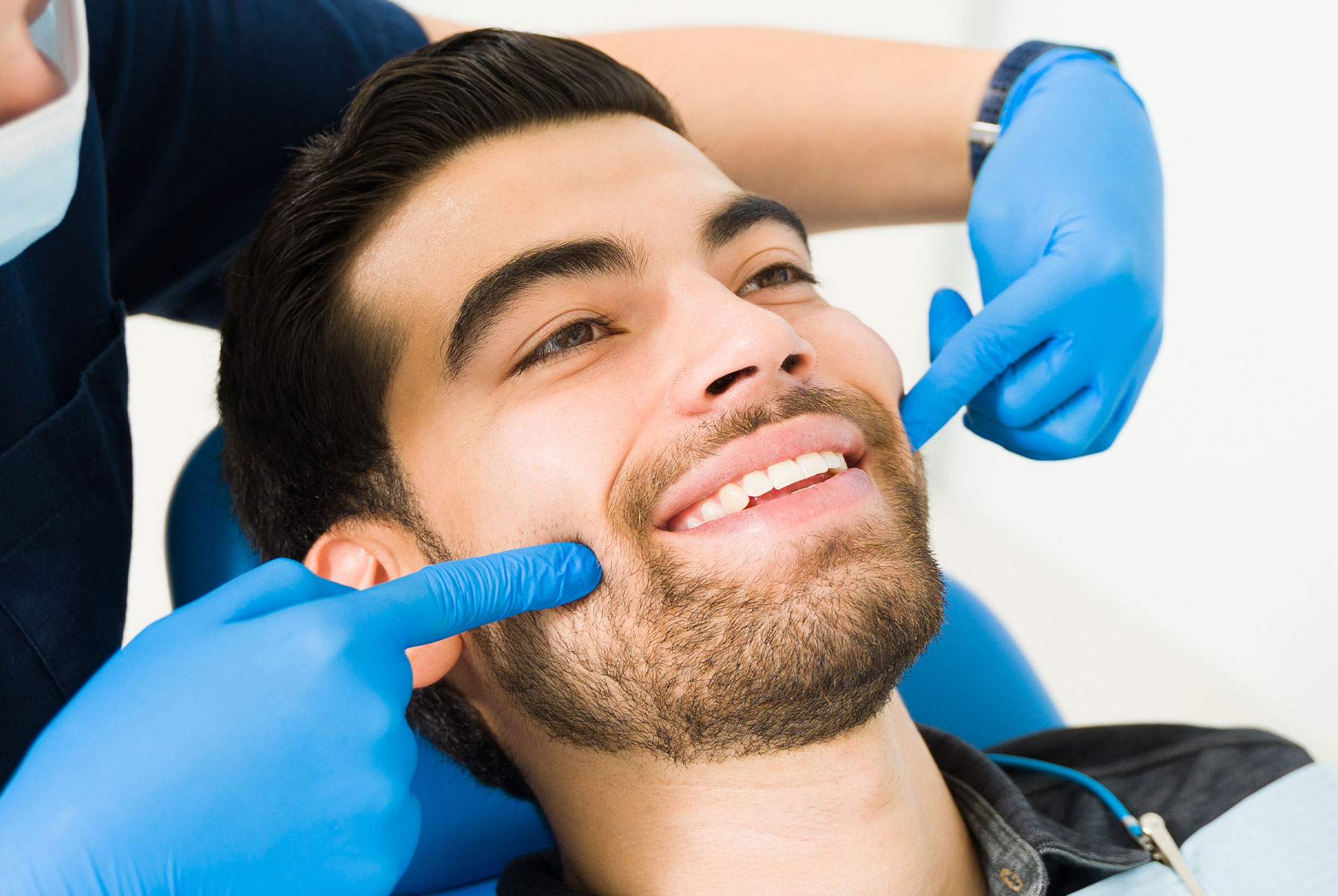 The image shows a man sitting in a dental chair, receiving dental care with a smile on his face.