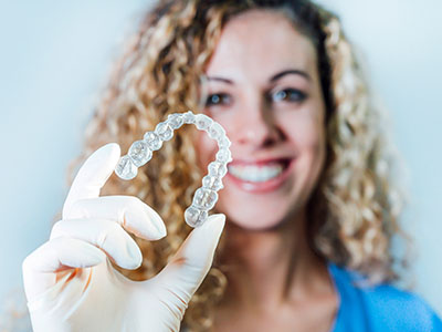 A woman holding a transparent dental retainer in her hand.