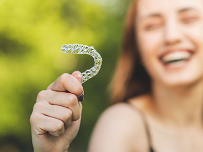 A smiling woman holding a transparent plastic dental retainer, showcasing its shape and transparency.