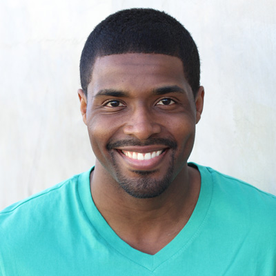 This image depicts an older couple, a man and a woman, embracing each other with smiles on their faces. They are seated outdoors during the daytime, with a clear sky in the background. The man is wearing a patterned shirt and has white hair, while the woman has gray hair and is dressed in a blue top. They both appear to be enjoying a moment of happiness together.