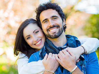 The image shows a man and a woman posing together, smiling at the camera.