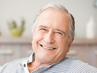 The image depicts an older man with a smile, sitting in a relaxed posture.